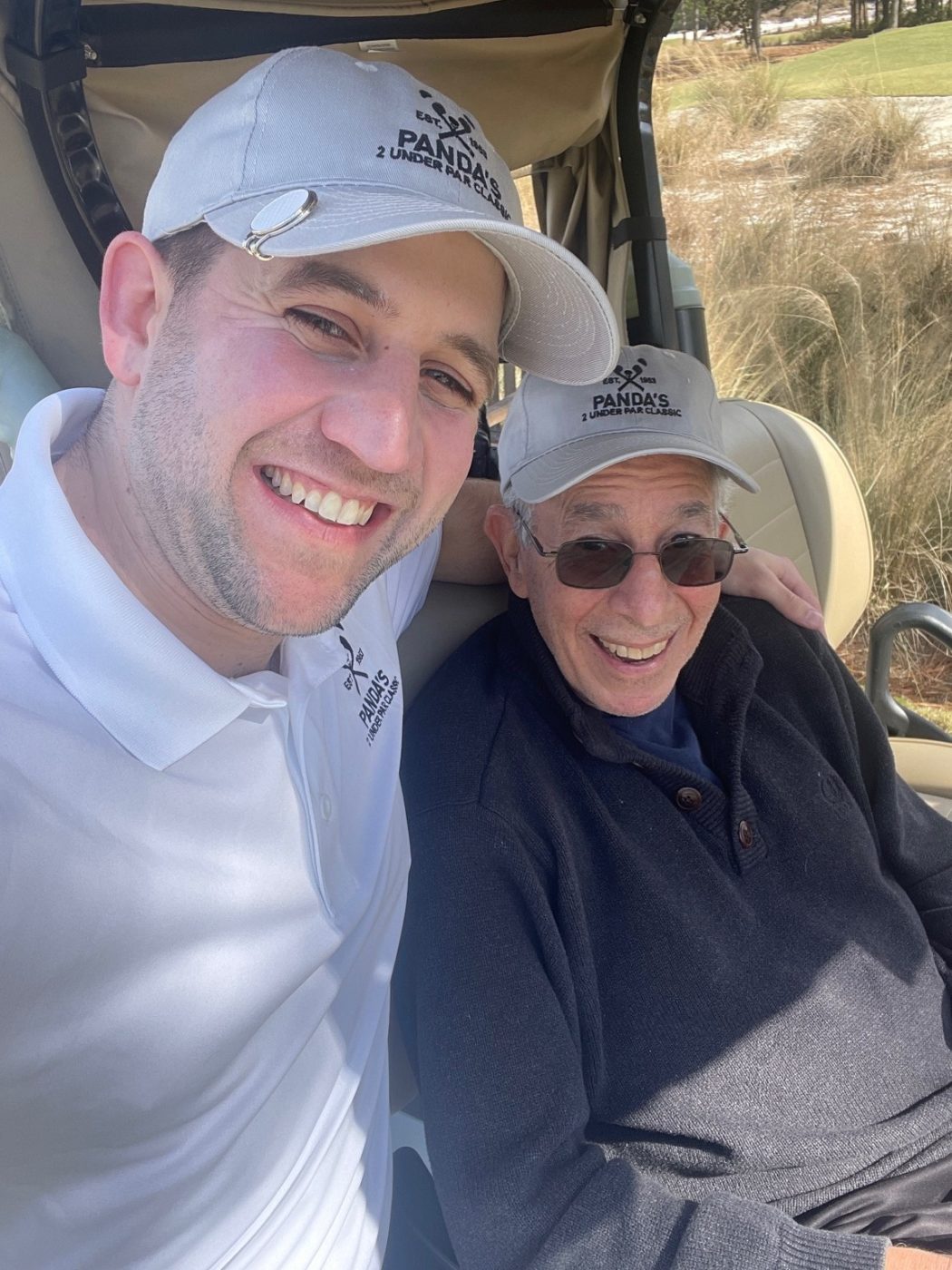 Two people pose for a photo in a golf cart on the golf course.